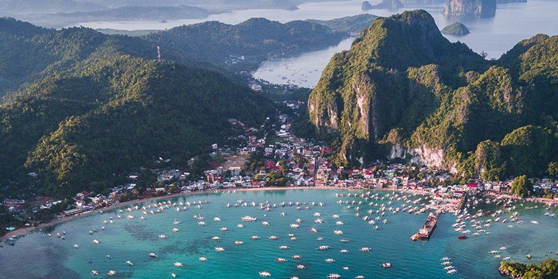 Le village d'El Nido vu du ciel, adossé à la falaise de Taraw, bateaux alignés dans la baie
