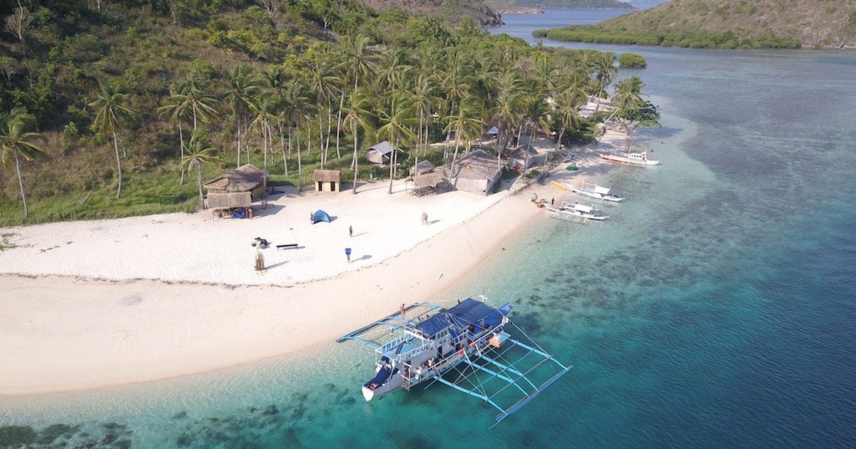Petit camp sur une plage d'île à Palawan, bangka amarrée devant le sable blanc